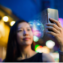Young Asian woman using face recognition software via smartphone, in front of colourful neon signboards in busy downtown city street at night. Biometric verification and artificial intelligence concept